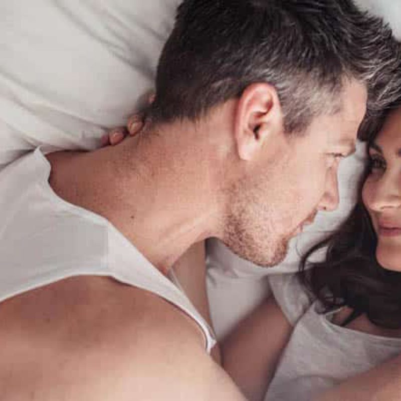 Overhead close up of young couple lying in bed together. Romantic couple in love looking at each other.